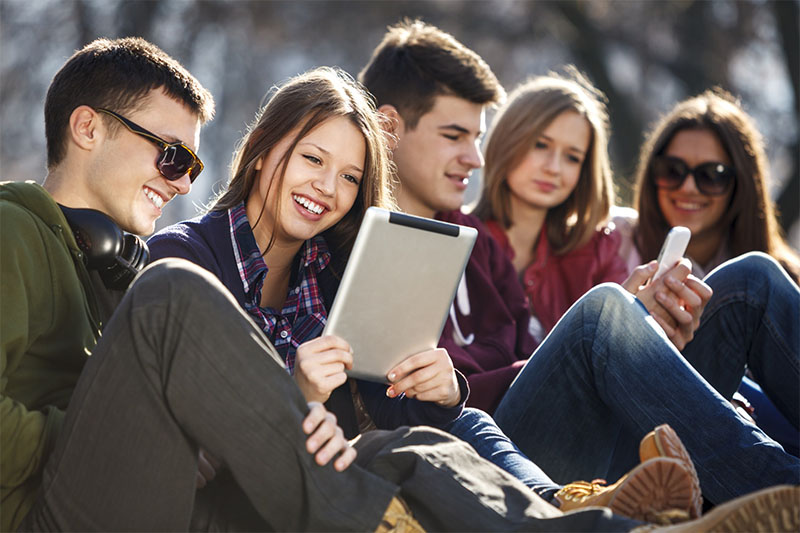 Young and happy teenagers using digital tablet and smart phone outdoors.
